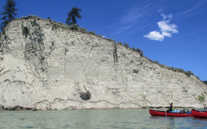 two canoes are paddled on calm water beside a tall white cliff